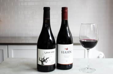 Two bottles of red wine next to a glass of the same.