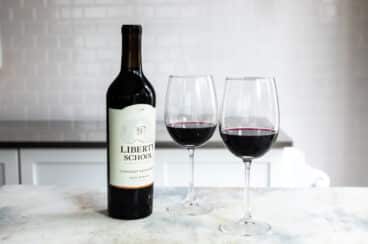 A bottle of red wine next to 2 glasses of the same.