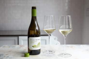 A bottle of white wine next to two glasses of the same.