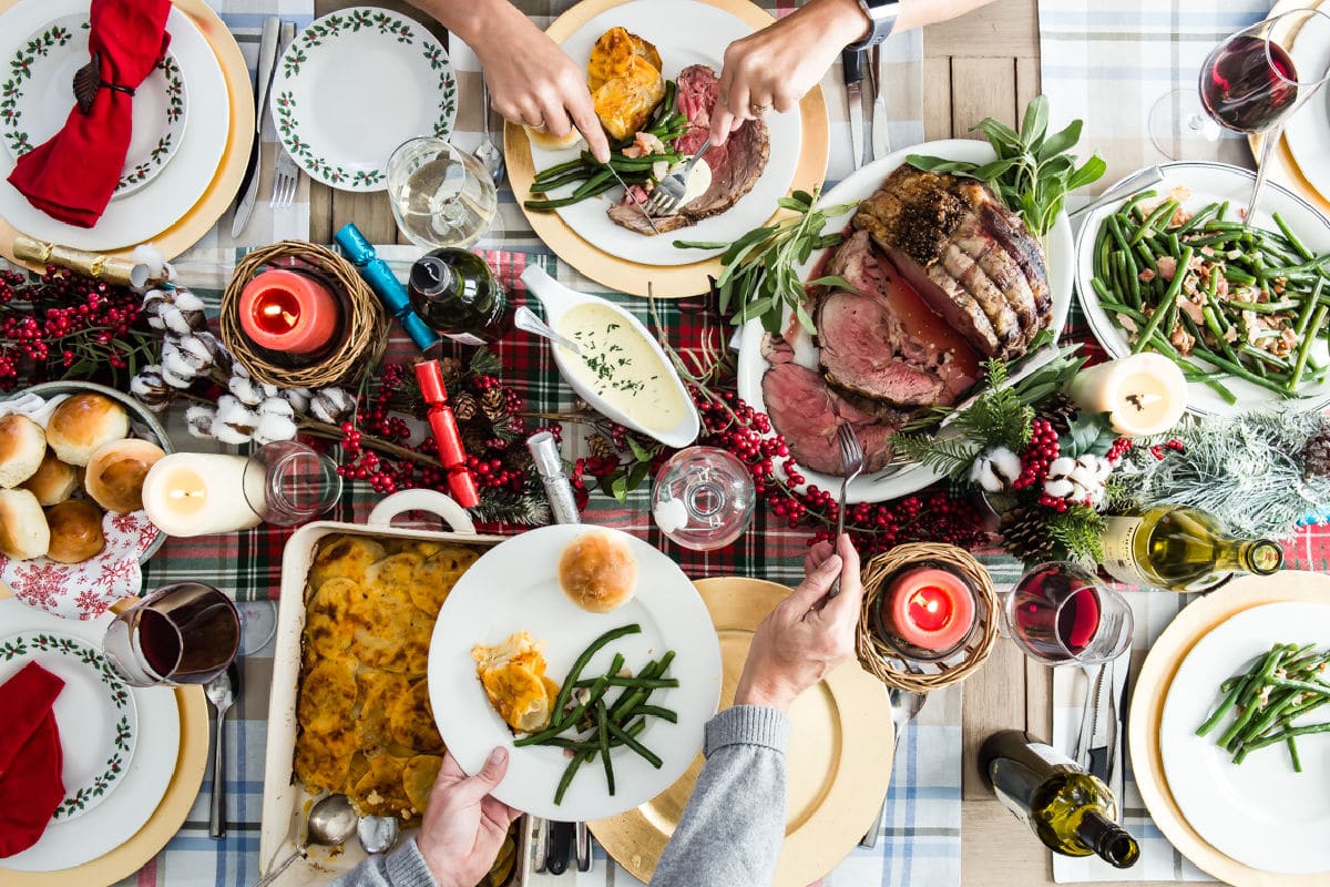 A Christmas table with prime rib, scalloped potatoes, green beans, and rolls.