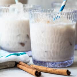 Three glasses of Agua de Horchata with cinnamon sticks in front of them.