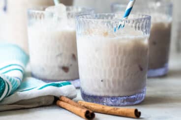 Three glasses of Agua de Horchata with cinnamon sticks in front of them.