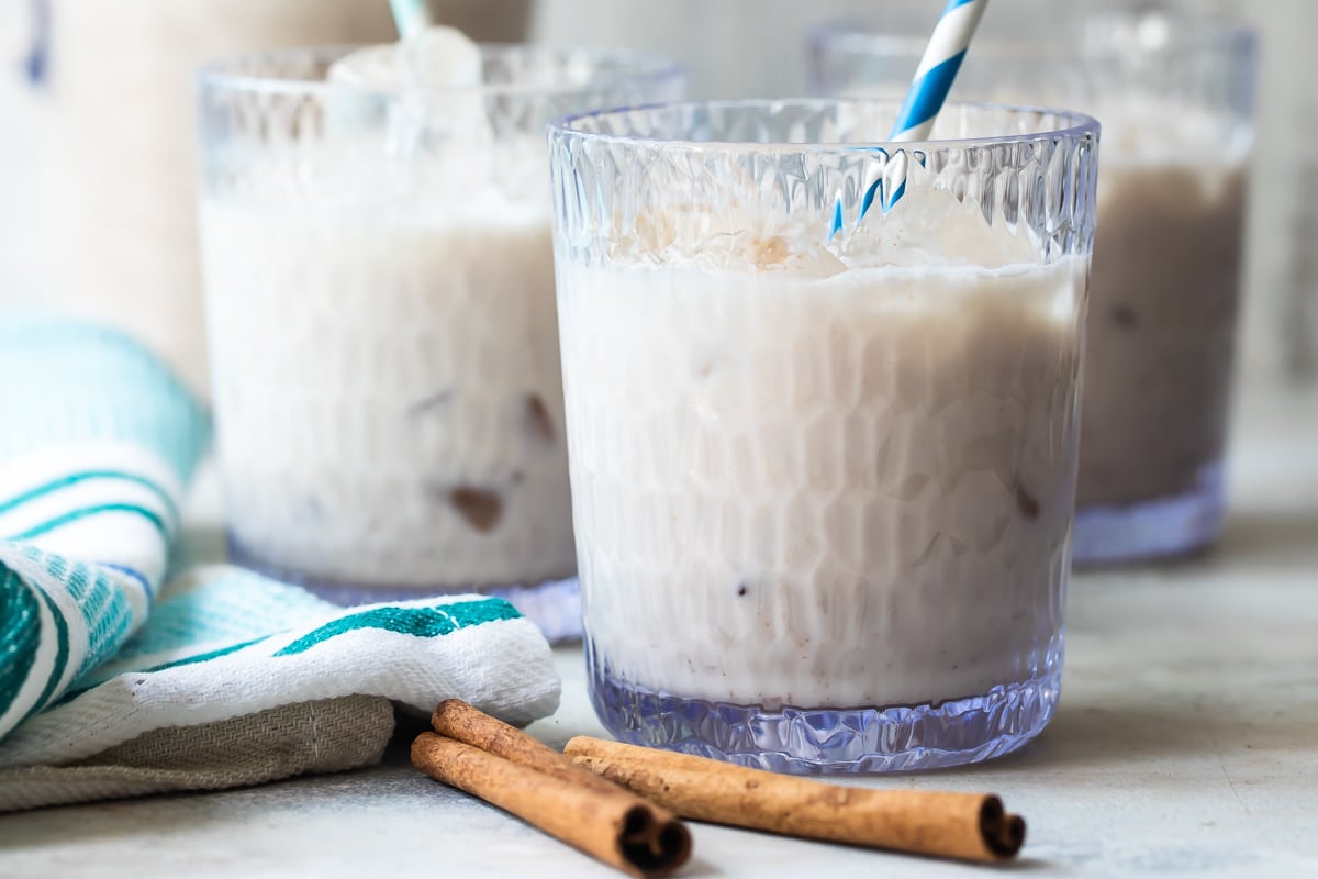 Three glasses of Agua de Horchata with cinnamon sticks in front of them.