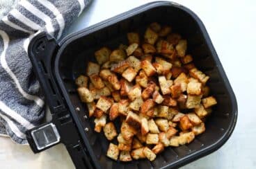 An air fryer basket with croutons in it.