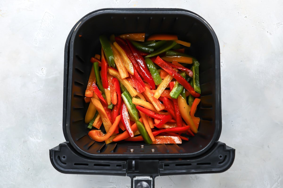 Pepper slices in an air fryer basket before being air fried.