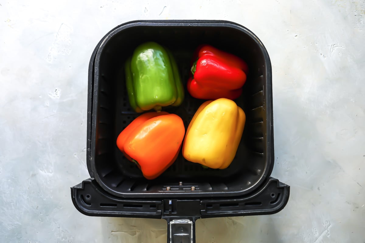 Four whole peppers in an air fryer basket.