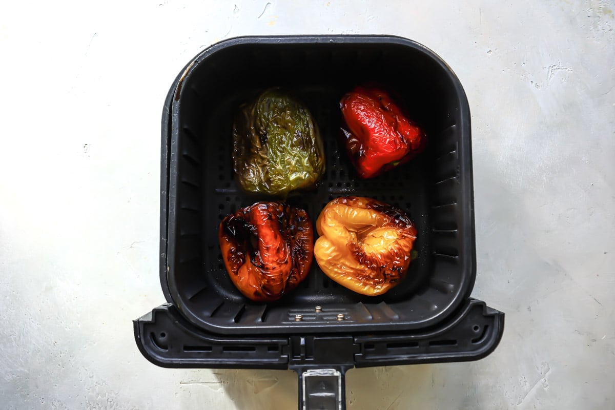 Four peppers in an air fryer basket after being air fried.