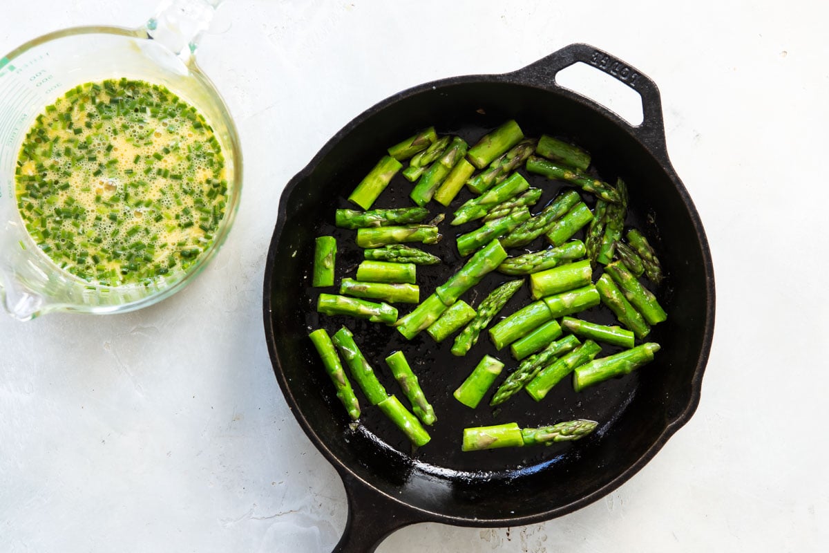Asparagus being cooked in a black cast iron skillet.
