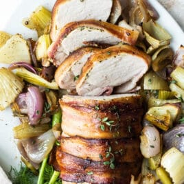 Bacon wrapped pork tenderloin surrounded by roasted fennel and onions.