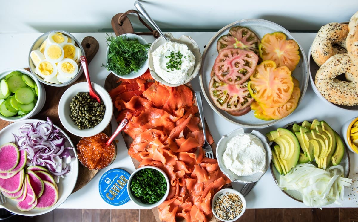 A Bagel Bar stocked with bagels, smoked salmon, cream cheese, avocado, tomatoes, watermelon radishes, cucumbers, caviar, and fresh herbs and spices.