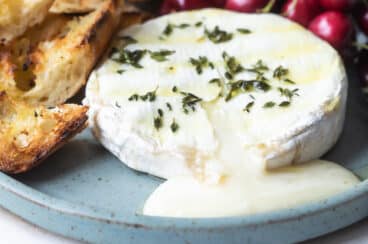 Baked brie on a blue plate with cherries and toasted bread pieces.