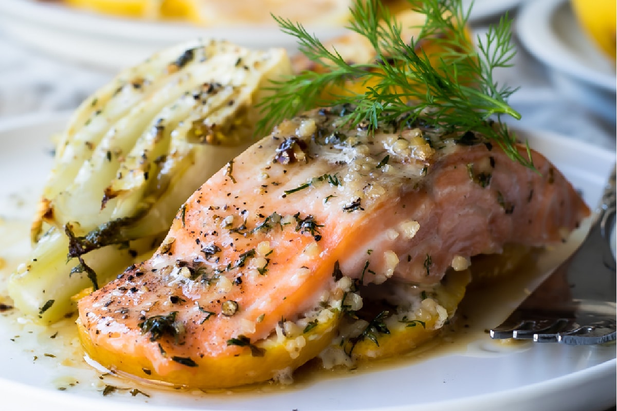A baked salmon filet on a plate next to roasted fennel.