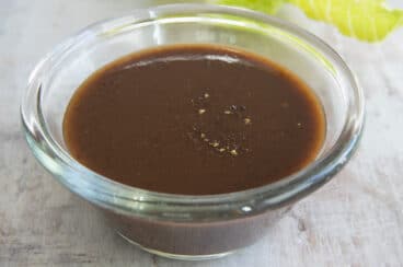 Balsamic Vinaigrette in a clear glass dish next to leafs of romaine lettuce.