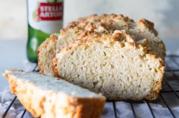 A loaf of beer bread cut into slices on a cooling rack.