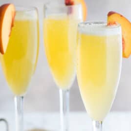 Three bellinis garnished with fresh peach slices.