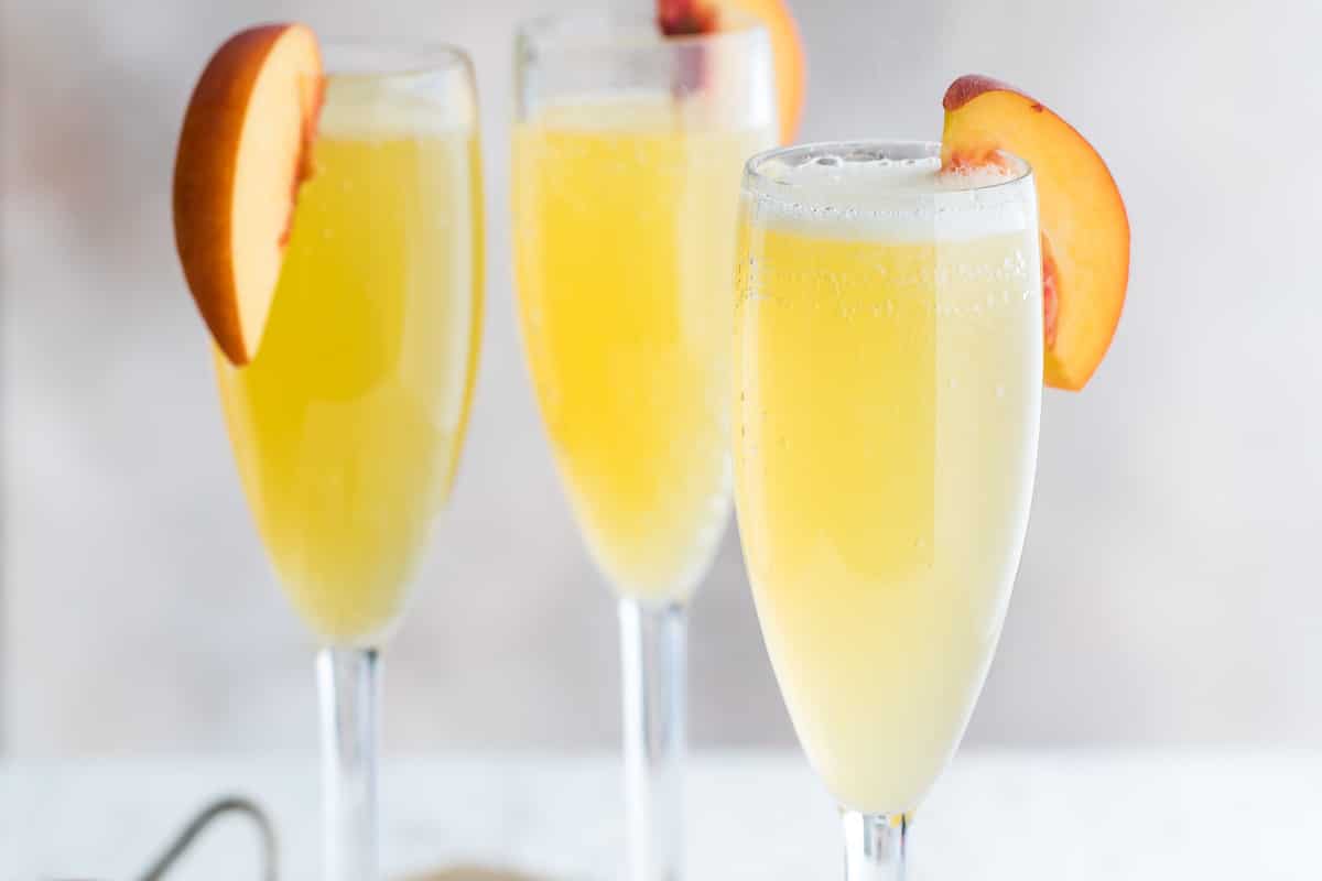 Three bellinis garnished with fresh peach slices.