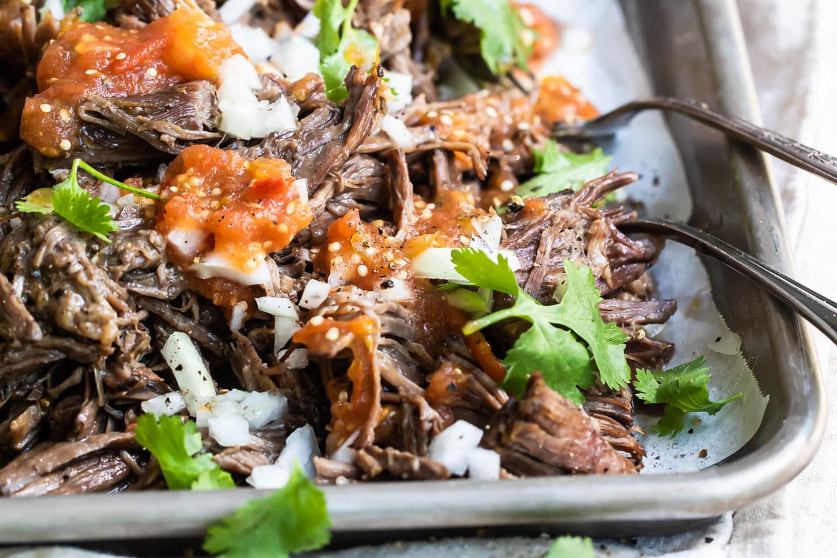 Garnished birria on a silver baking sheet.