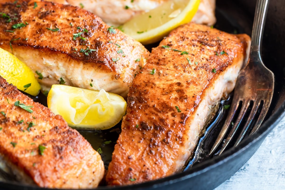 Salmon in a cast iron skillet with lemons for garnish.