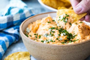 Someone dipping a tortilla chip in buffalo chicken dip.