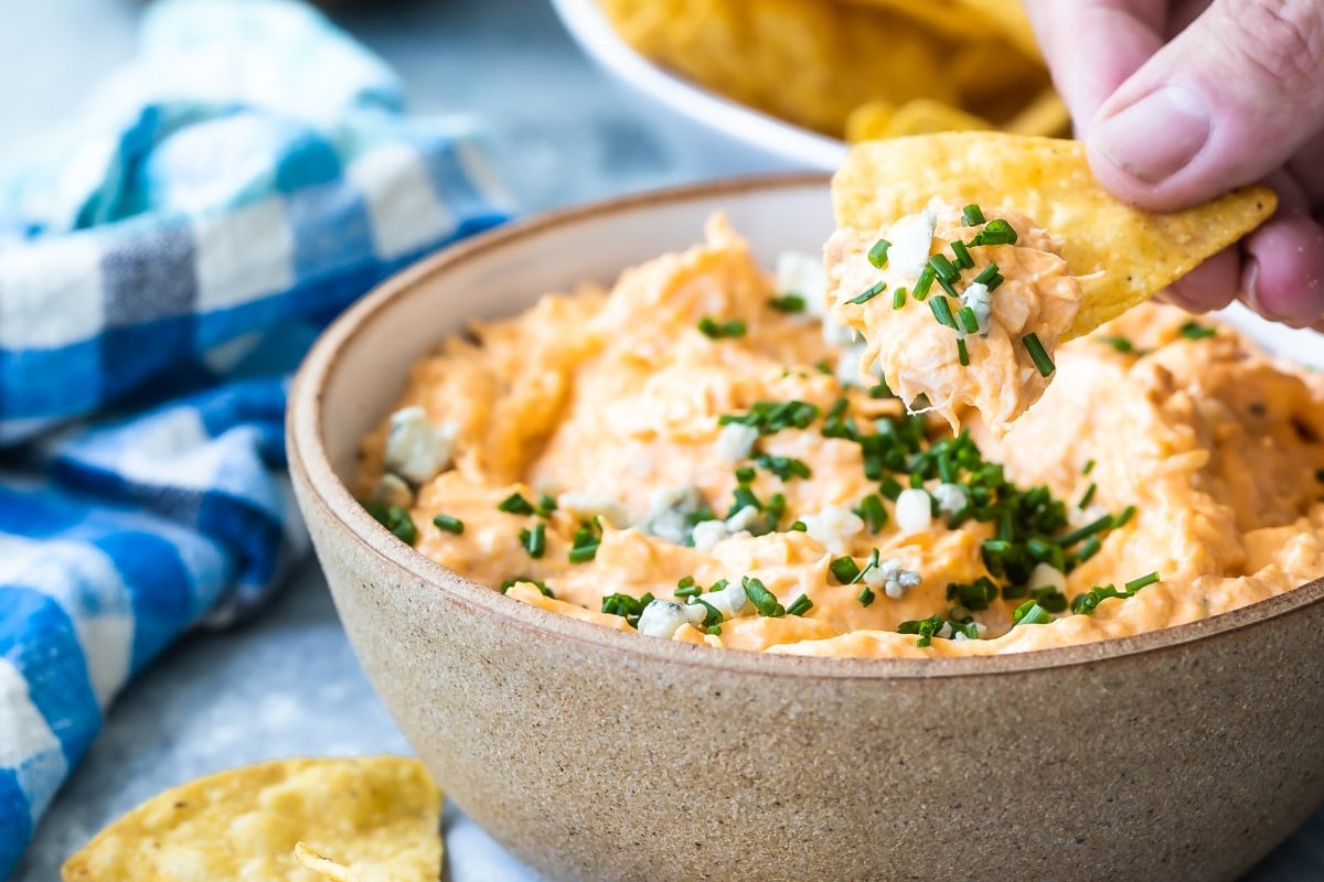 Someone dipping a tortilla chip in buffalo chicken dip.