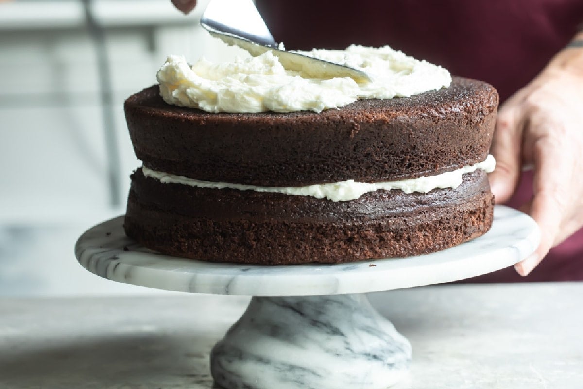 Buttercream frosting being spread on a chocolate layer cake.