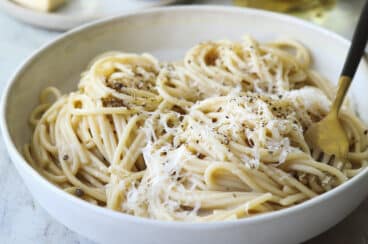 Someone taking a fork of Cacio e pepe out of a white bowl.