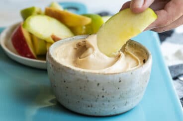 An apple being dipped in caramel apple dip.