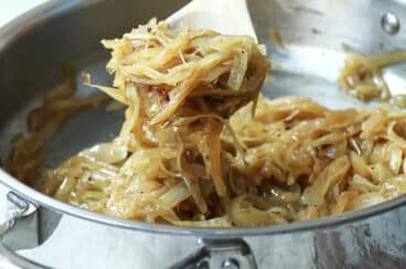 Someone scooping out a spoonful of caramelized onions out of a metal skillet.