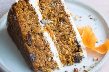 A slice of carrot cake on a blue plate with a candied carrot peel.