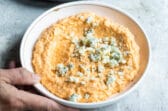 Someone setting down a bowl of cauliflower buffalo dip.
