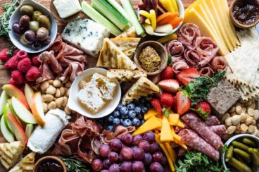 A charcuterie board filled with meats, cheese, fruits, nuts, crackers, and other snacks.
