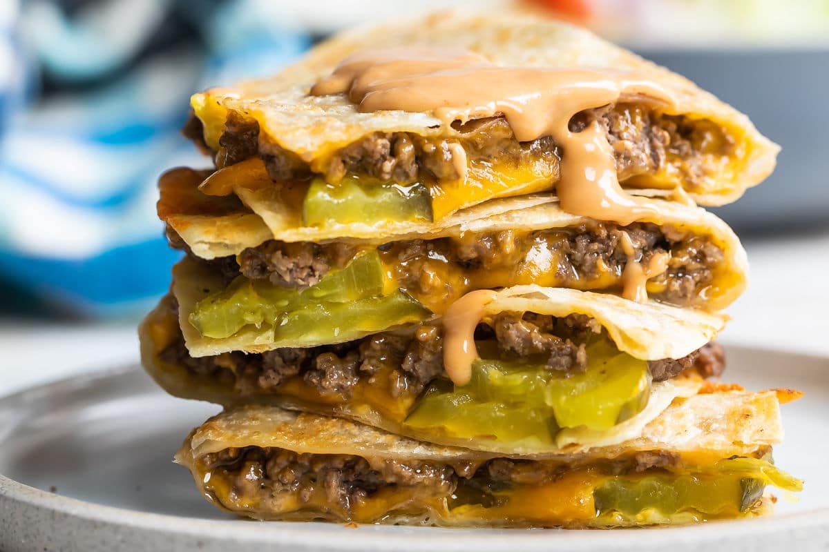 A cheeseburger quesadilla stacked on a plate with a wedge salad in the background.
