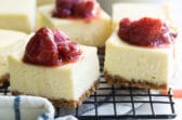 Cheesecake bars on a cooling rack topped with strawberry topping.