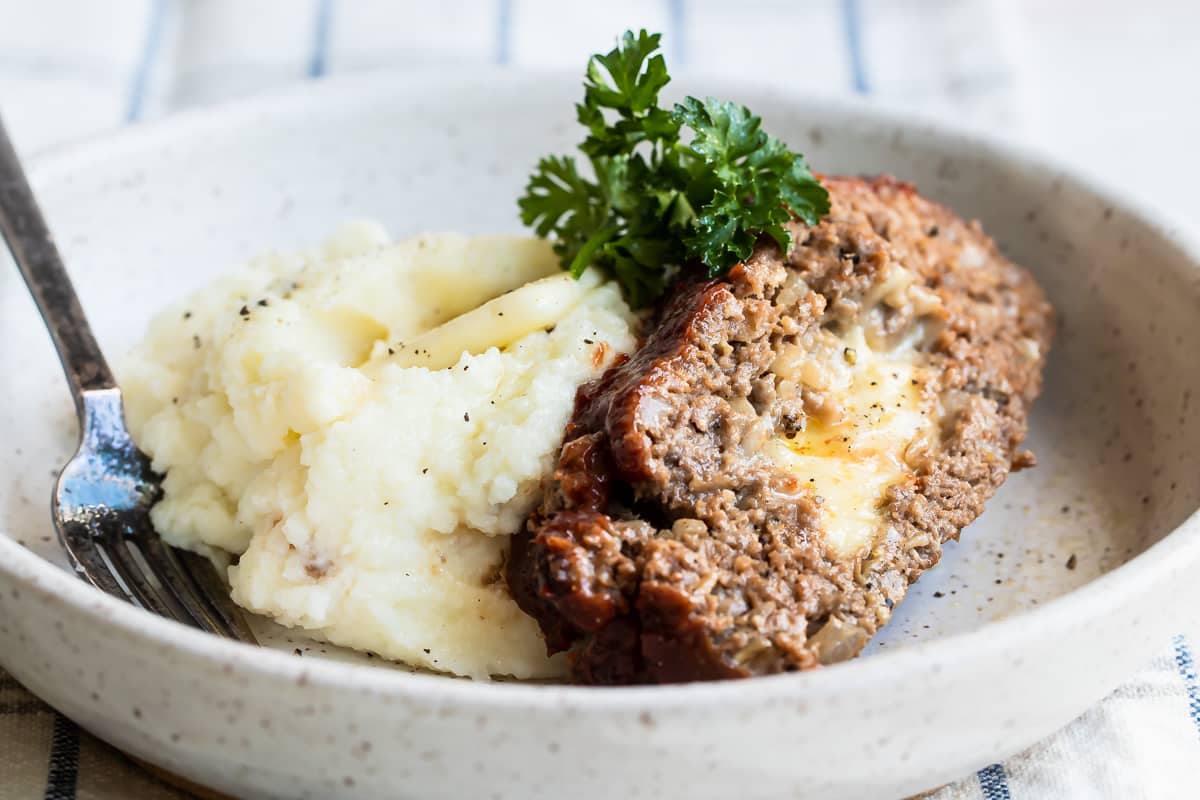 A slice of cheesy meatloaf with mashed potatoes in a low gray bowl.