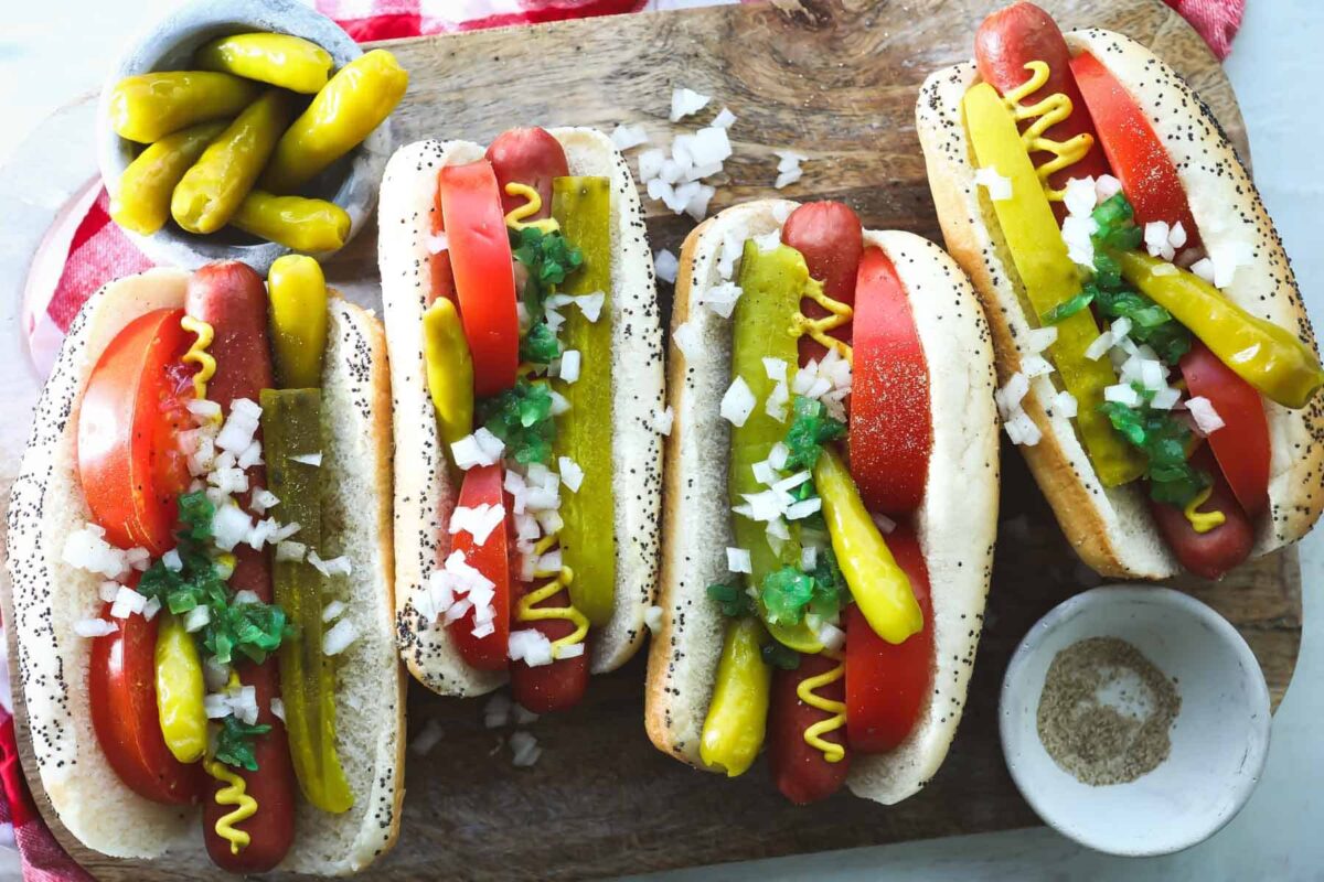 Four Chicago style hot dogs on a wooden platter.