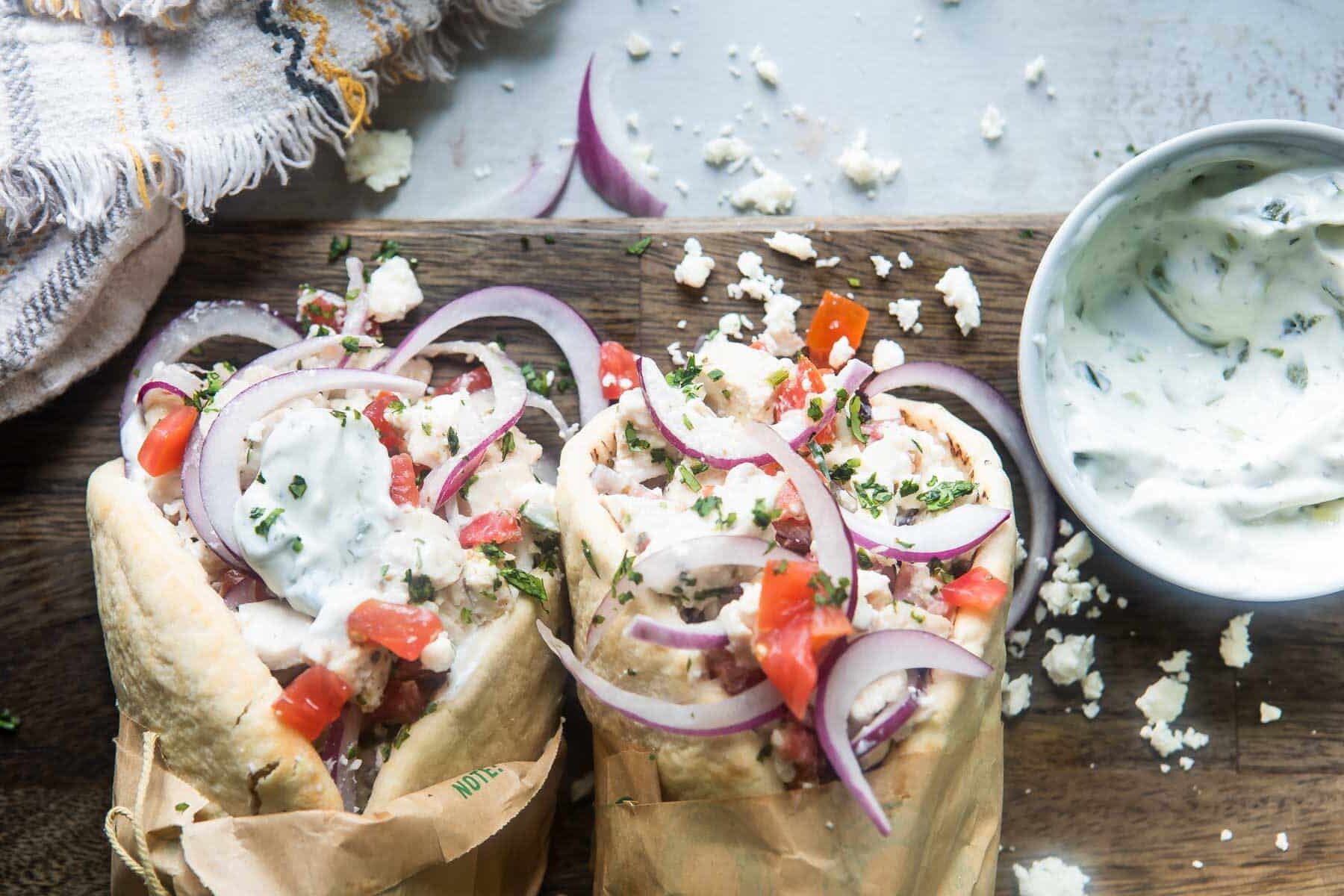 Two chicken gyros on a wooden cutting board.