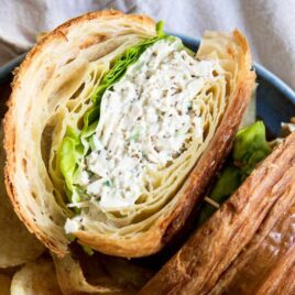A chicken salad sandwich on a croissant with chips next to it.