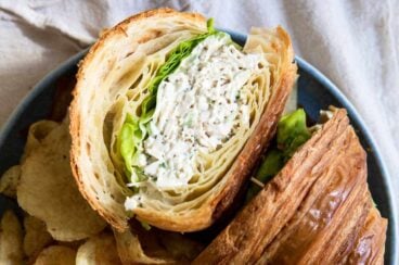A chicken salad sandwich on a croissant with chips next to it.