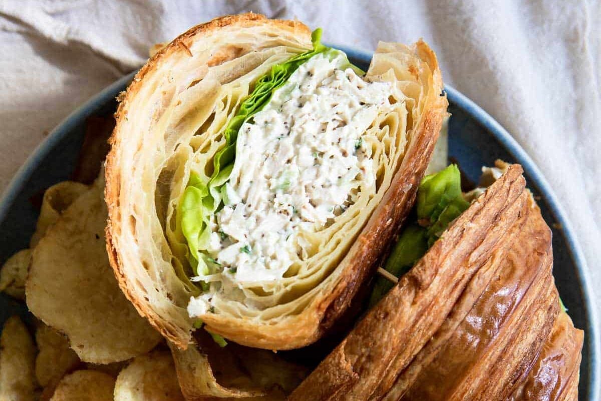 A chicken salad sandwich on a croissant with chips next to it.