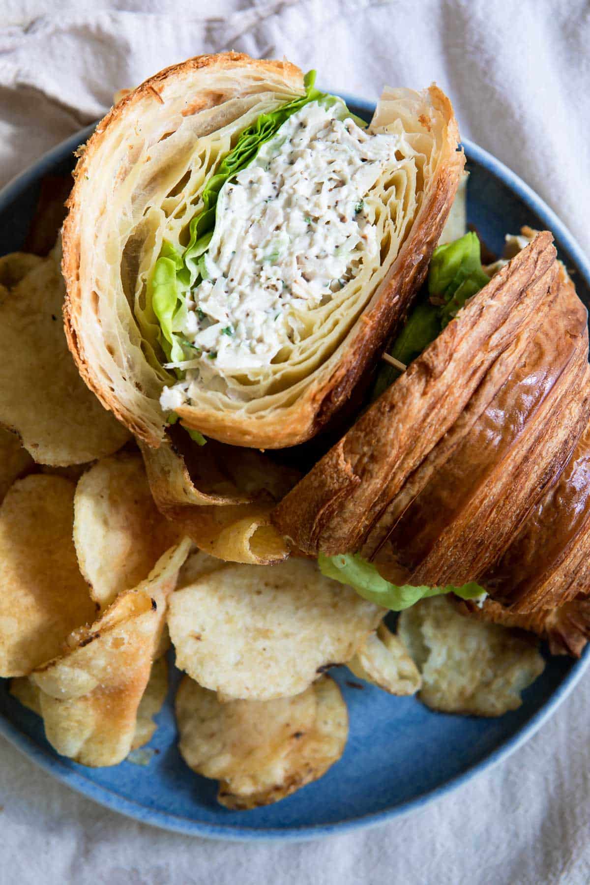 A chicken salad sandwich on a croissant with chips next to it.