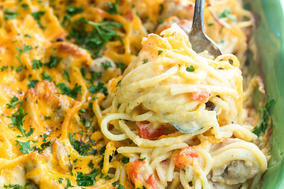 Chicken spaghetti being scooped out of a green casserole dish.