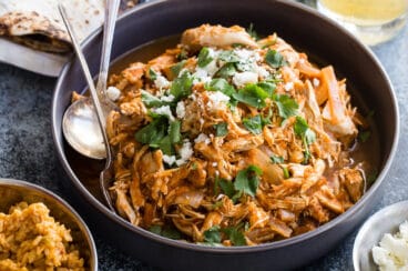 Chicken tinga in a bowl with tortilla shells and lettuce nearby.