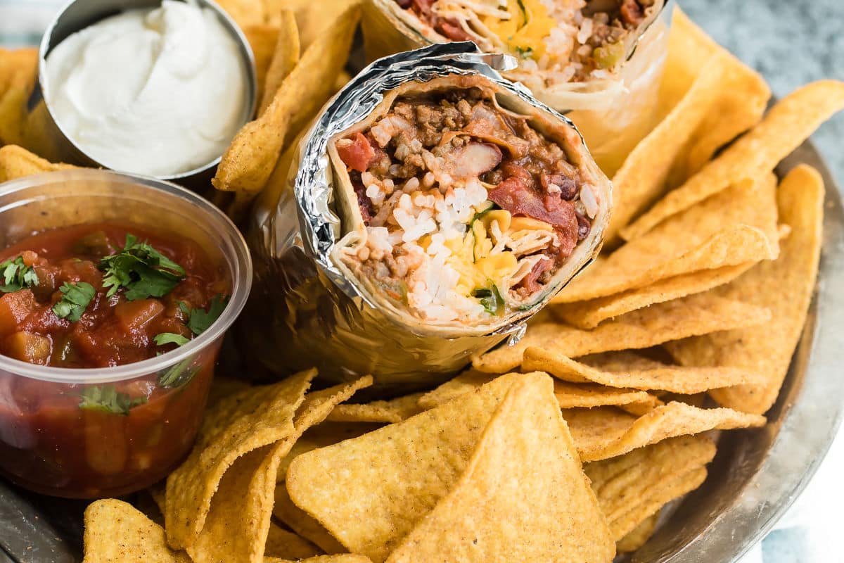 A chili cheese burrito sliced open to show the insides on a pile of tortilla chips.