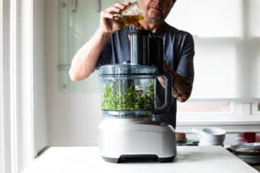 Someone making chimichurri sauce in a food processor.