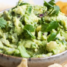 Chipotle guacamole in a serving dish on a white platter with tortilla chips.
