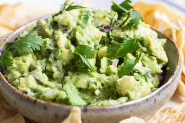 Chipotle guacamole in a serving dish on a white platter with tortilla chips.
