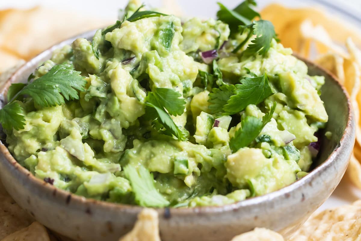 Chipotle guacamole in a serving dish on a white platter with tortilla chips.