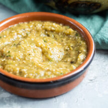 Chipotle tomatillo green chili salsa in a red bowl and a bowl of chips.