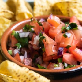 Chipotle tomato salsa in a black bowl on a blue plate with tortilla chips.
