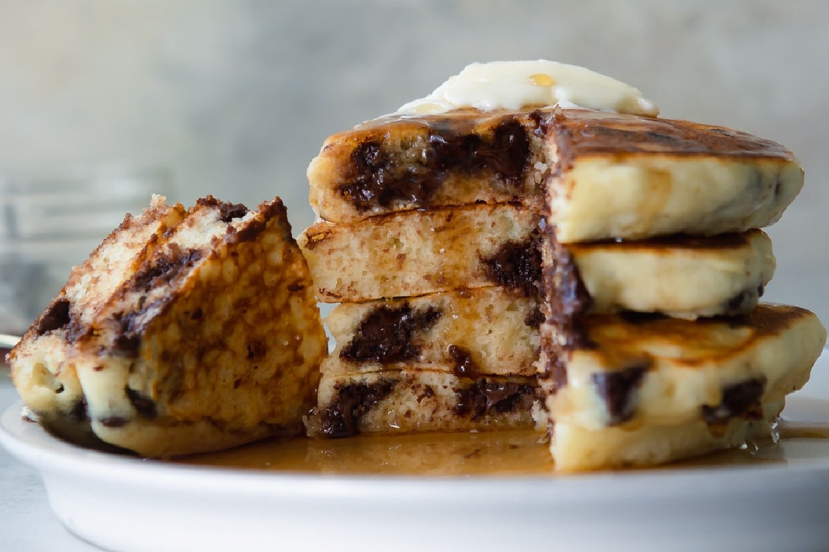 A stack of four chocolate chip pancakes on a plate.